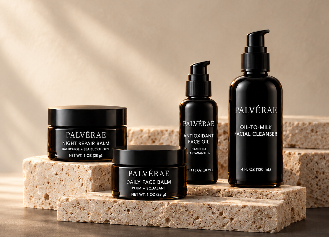 Four black Palvérae skincare containers arranged on stacked natural stone blocks against a warm beige studio background with soft shadows. The products include a night repair balm, daily face balm, antioxidant face oil, and oil-to-milk facial cleanser.
